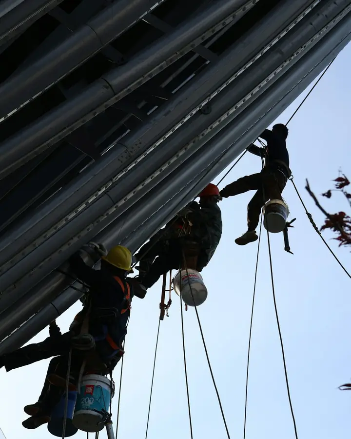Workers on ropes painting a tall steel structure